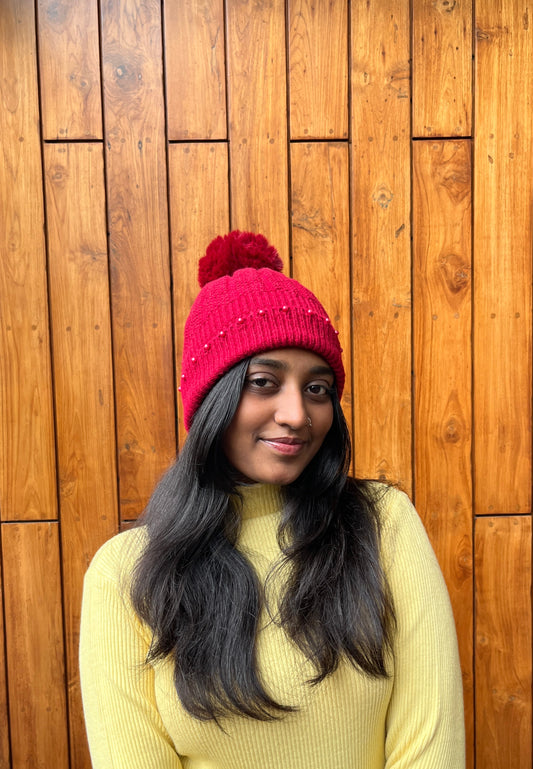 Woman wearing a red woollen pom-pom cap with bead detailing – Madhuri Woollens