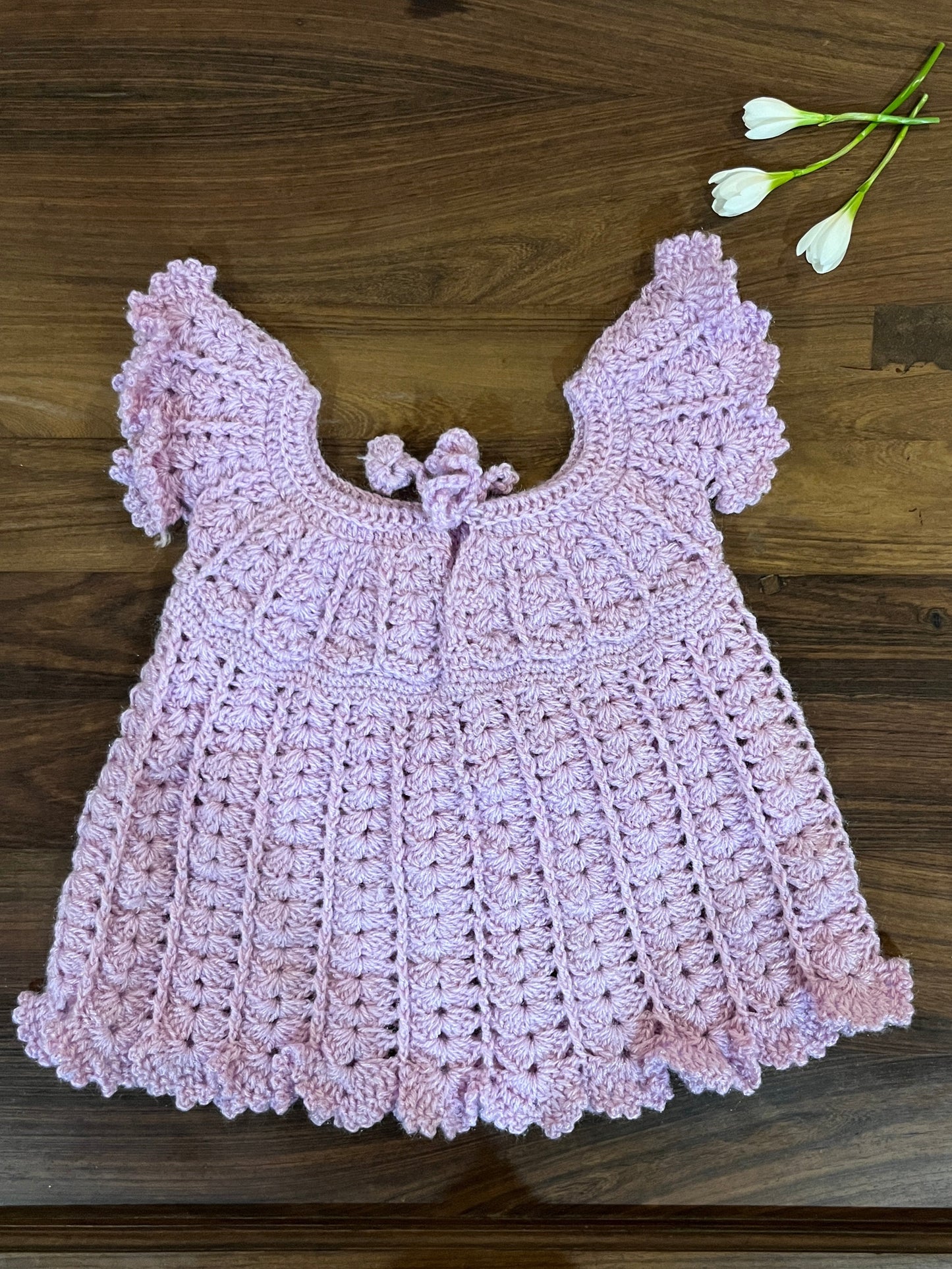 Soft pink handmade crochet baby dress with shell stitch and flutter sleeves for infants aged 12 to 18 months