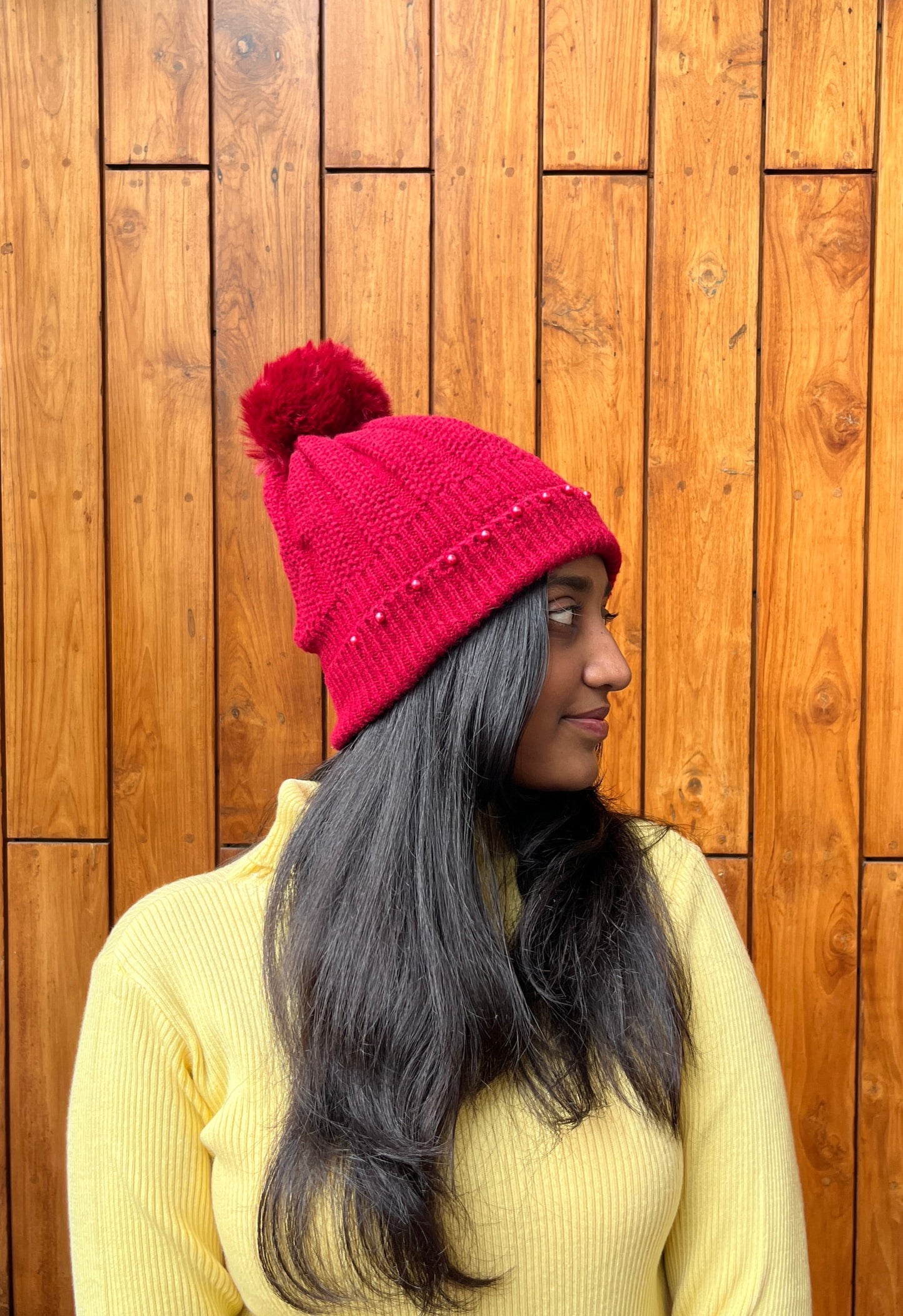 Woman wearing a red woollen pom-pom cap with bead detailing – Madhuri Woollens