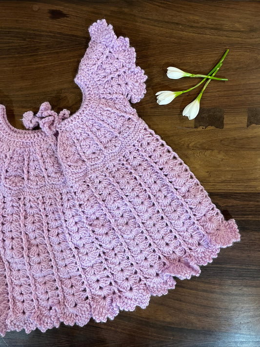 Soft pink handmade crochet baby dress with shell stitch and flutter sleeves for infants aged 12 to 18 months.